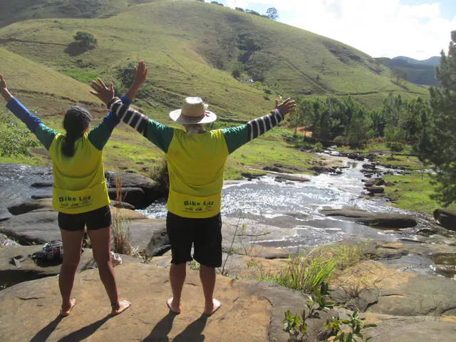 Dois caminhantes diante de um curso de água e montanhas